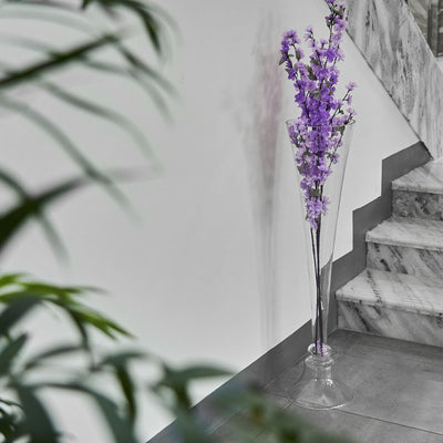 Purple flowers in a glass vase near a staircase.