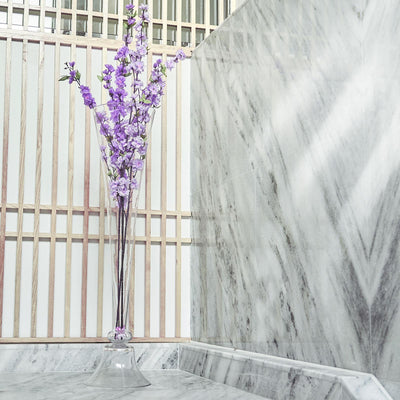 Elegant glass vase with purple flowers against a marble backdrop.