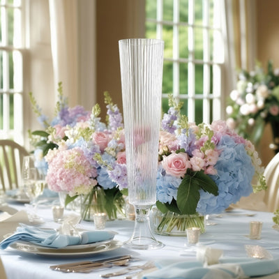 Elegant tall glass vase with textured design, surrounded by pastel flower arrangements.