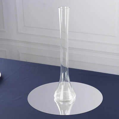 Clear glass vase on a reflective surface against a plain backdrop.