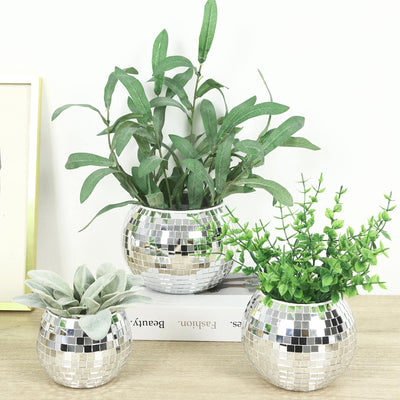 Three artificial potted plants in silver mosaic vases on a tabletop