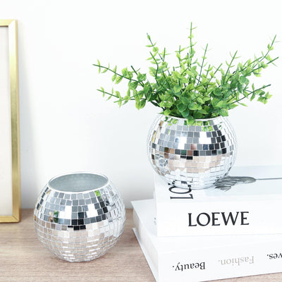 Silver mosaic vase with green artificial plant on decorative books