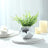 Silver mosaic vase with green artificial plant and candles on white table