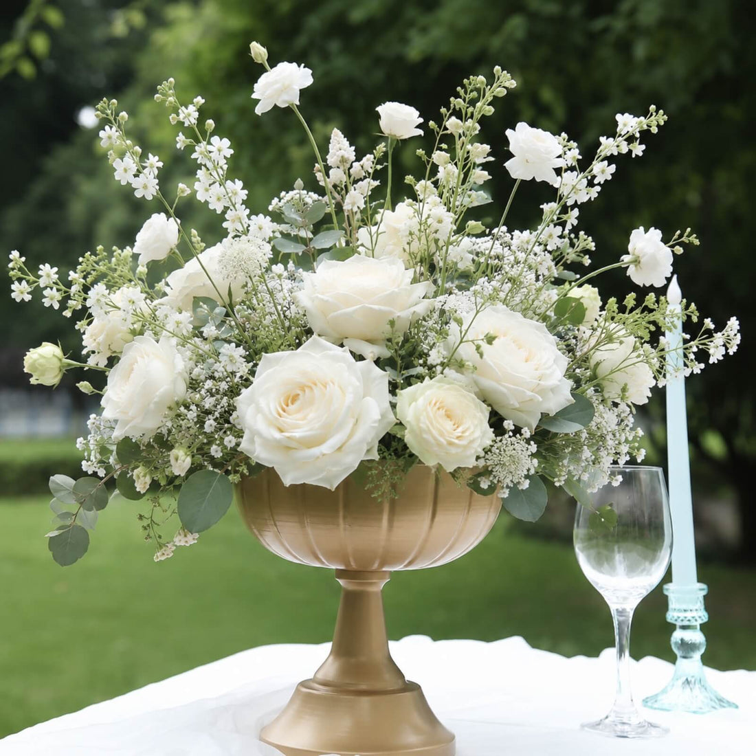 White rose floral centerpiece in gold vase with wine glass and candle outdoors