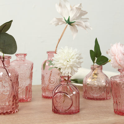 Assorted vintage pink glass vases with flowers on a wooden table.