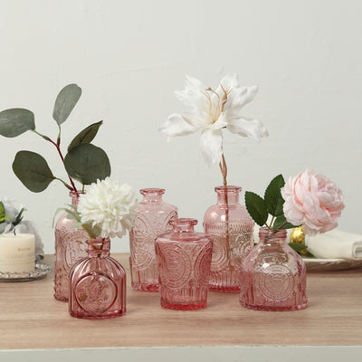 Decorative pink glass vases with flowers on a wooden table.
