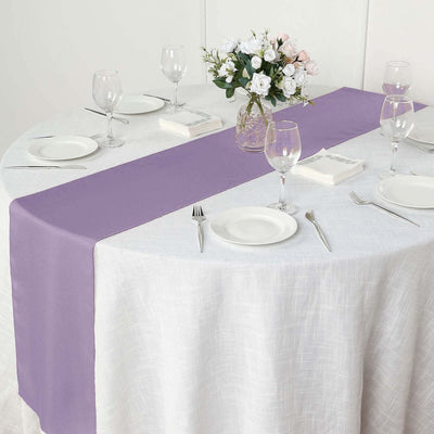 Purple table runner on a round table set for dining with flowers and glassware.
