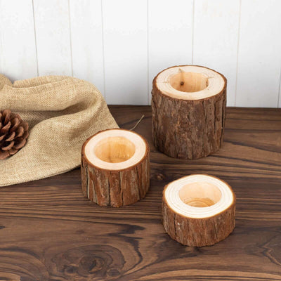 Natural wood candle holders in three sizes on a rustic wooden surface.