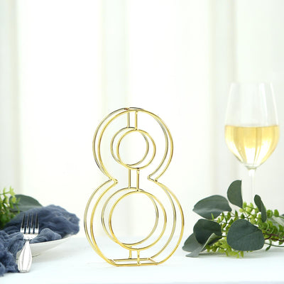 Gold number 8 table centerpiece with wine glass and greenery backdrop.