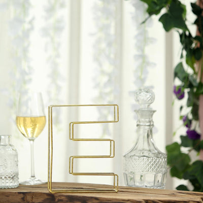 Gold geometric wire vase on a rustic wooden table with decorative background.