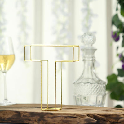 Gold wire letter T decor on wooden table with glassware in the background.