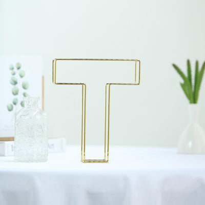 Gold letter T decorative piece on a white table with minimal decor.