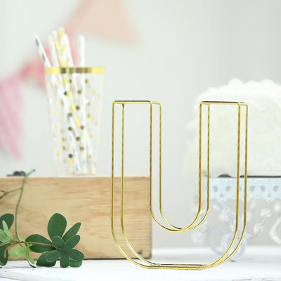 Gold letter U decor with green leaves in a styled setting.
