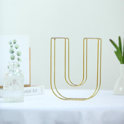 Gold wire letter U decor on a white table with plants in the background.