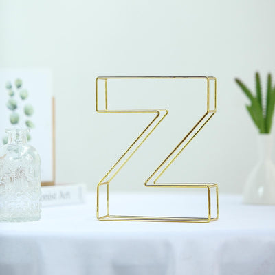 Gold wire letter Z sculpture on a white table with decorative plants in the background.
