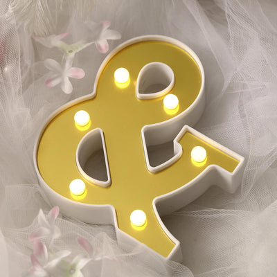Yellow "&" marquee light with LED bulbs on a soft fabric background.