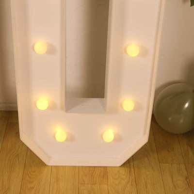 Vintage marquee letter "U" with glowing bulbs on a wooden floor.