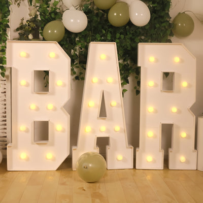 Illuminated "BAR" letters with balloons and greenery backdrop.