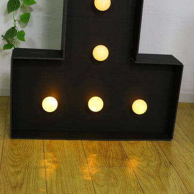 Light-up letter sign with warm bulbs on a wooden floor.