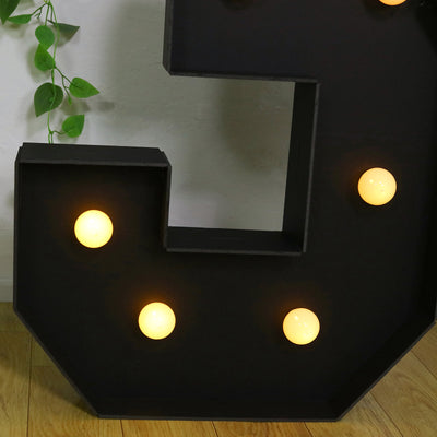 Black marquee letter "C" with warm glowing bulbs