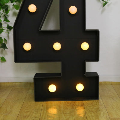 Black marquee number 4 with glowing lights on a wooden floor.
