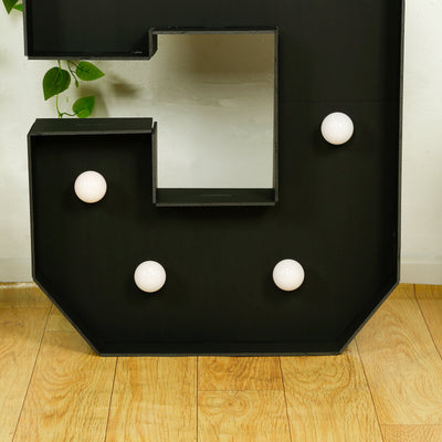Black marquee letter 'C' with round light bulbs on a wooden floor.