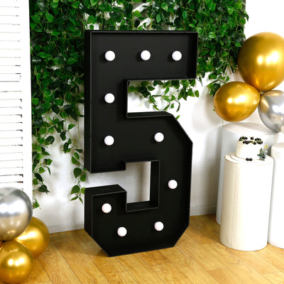 Black marquee number five with light bulbs, surrounded by greenery and balloons.