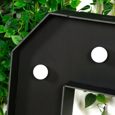 Black decorative letter with white circular accents against greenery