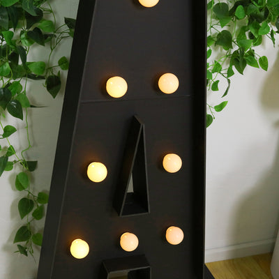 Decorative marquee letter with lights and greenery backdrop.