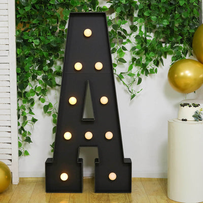 Decorative marquee letter A with lights and greenery backdrop