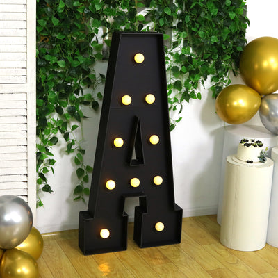 Decorative marquee letter "A" with lights, surrounded by greenery and balloons.