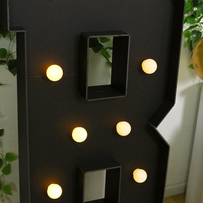 Light-up marquee letter with glowing bulbs on a black background.