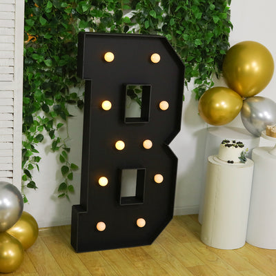 Large illuminated letter "B" surrounded by greenery and balloons.
