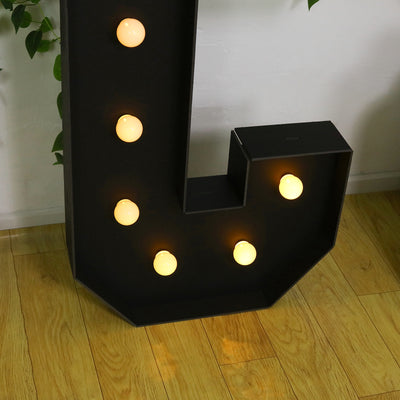 Decorative marquee letter 'J' with warm glowing bulbs on a wooden floor.