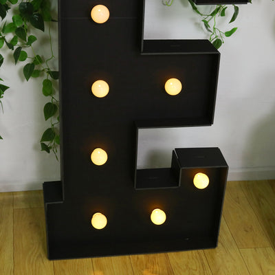 Black marquee letter "E" with lit bulbs on a wooden floor.