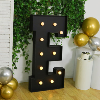 Large illuminated black letter "E" surrounded by greenery and balloons.