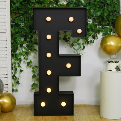 Light-up marquee letter E with bulbs, surrounded by greenery and balloons.
