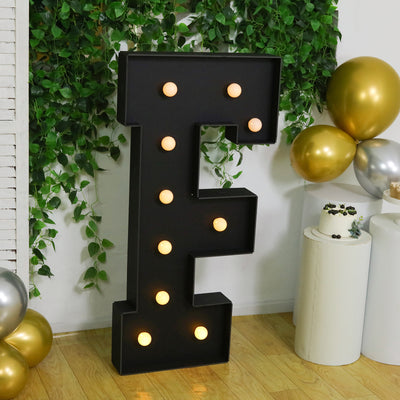 Illuminated black letter "E" marquee sign with light bulbs in a festive setting.