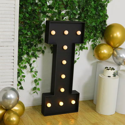Large decorative marquee letter 'I' with lights, surrounded by greenery and balloons.