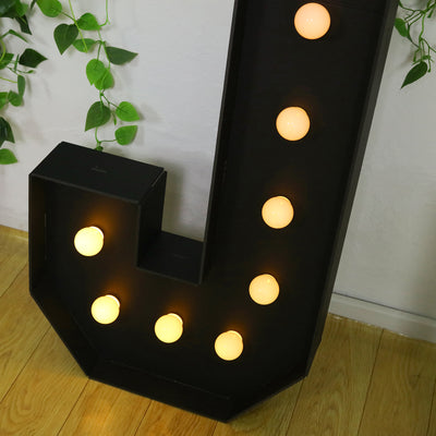 Black marquee letter "J" with glowing bulbs, decorative lighting piece.