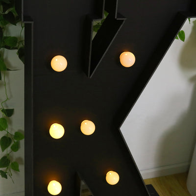 Black decorative letter "K" with warm white bulbs lit up.
