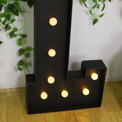 Decorative letter 'L' marquee light with glowing bulbs on a wooden floor.