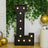 Large illuminated letter "L" decoration for events, surrounded by greenery and balloons.