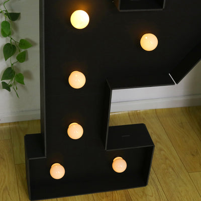 Black marquee letter "P" with illuminated bulbs on a wooden floor.