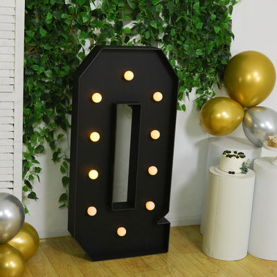Large black marquee letter "Q" with lights, set against greenery and balloons.