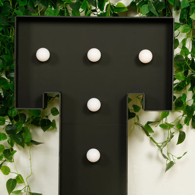 Black letter "T" marquee sign with white bulbs, surrounded by green vines.