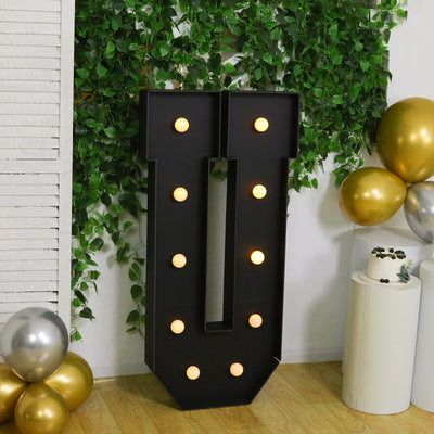 Black marquee letter "U" with lights, surrounded by greenery and festive decor.