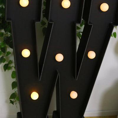 Black decorative letter "W" with warm glowing lights.
