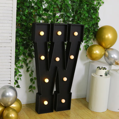 Decorative marquee letter "W" with lights, surrounded by greenery and balloons.