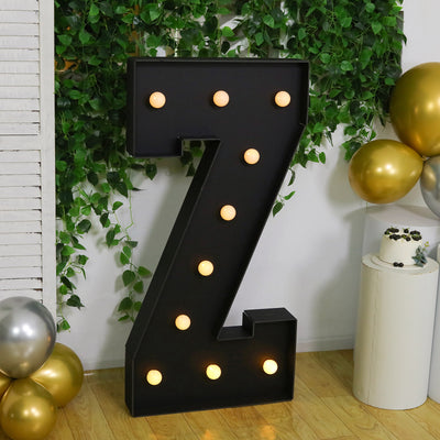 Large marquee letter "Z" with lights, surrounded by greenery and balloons.